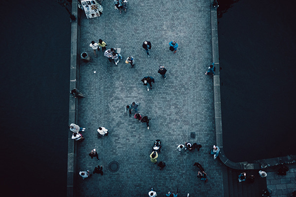 A high-angle camera shot of numerous people walking across a bridge.