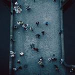A high-angle camera shot of numerous people walking across a bridge.