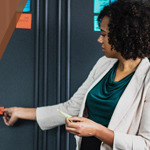 A female teacher placing an orange sticky note on the wall.